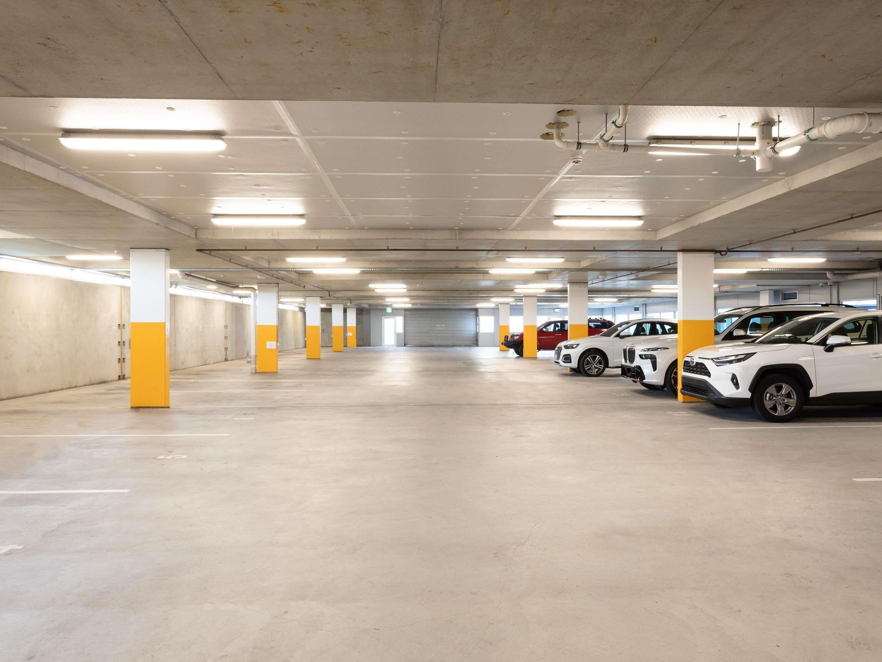 Eine mehrstöckige Parkgarage mit Betonpfeilern, Neonbeleuchtung und mehreren parkenden Autos.
