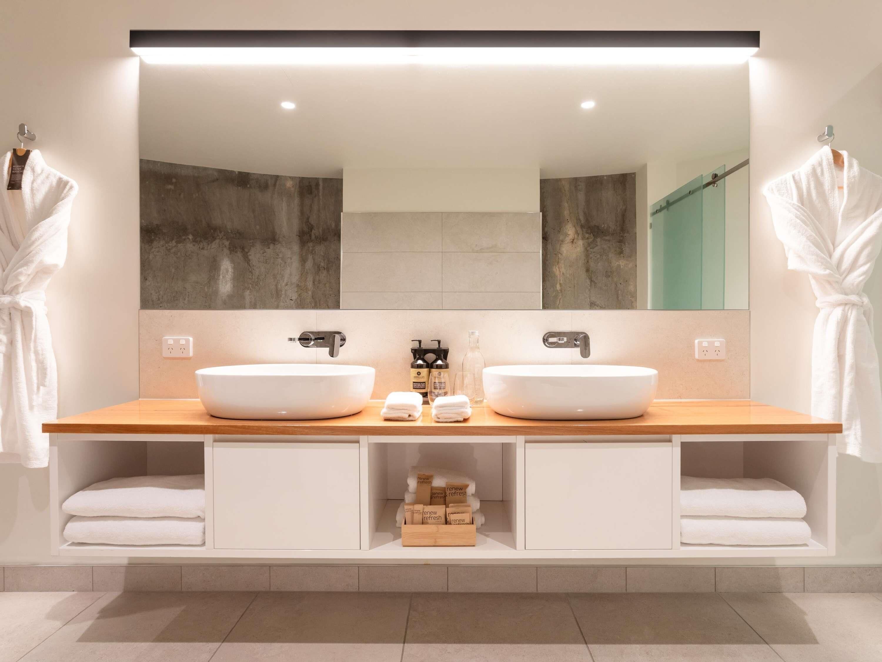A modern bathroom with two sinks, a large mirror, and a towel rack.