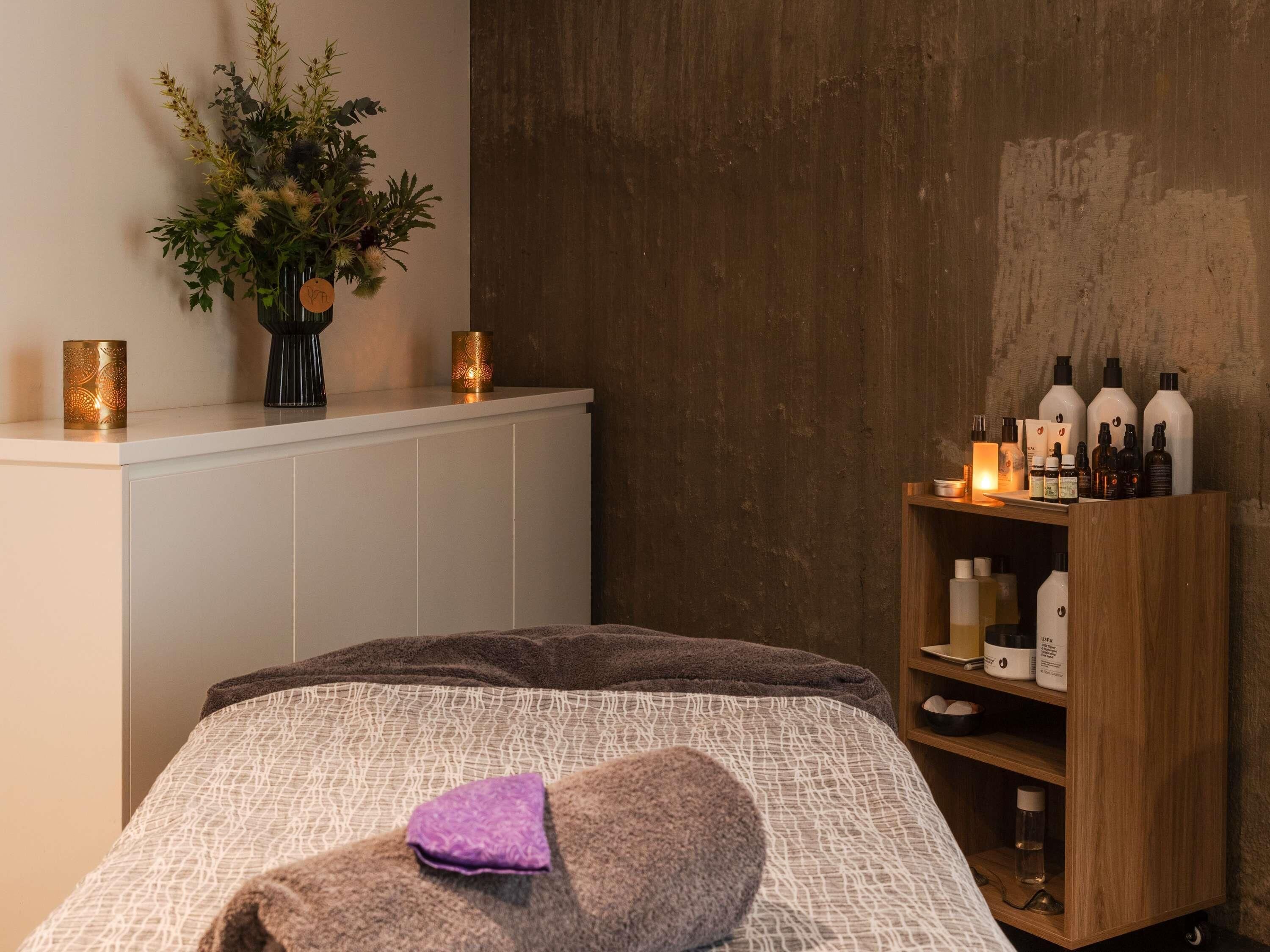 A neatly arranged bedroom with a bed, a bedside table with candles, a small plant, and a shelf with toiletries.