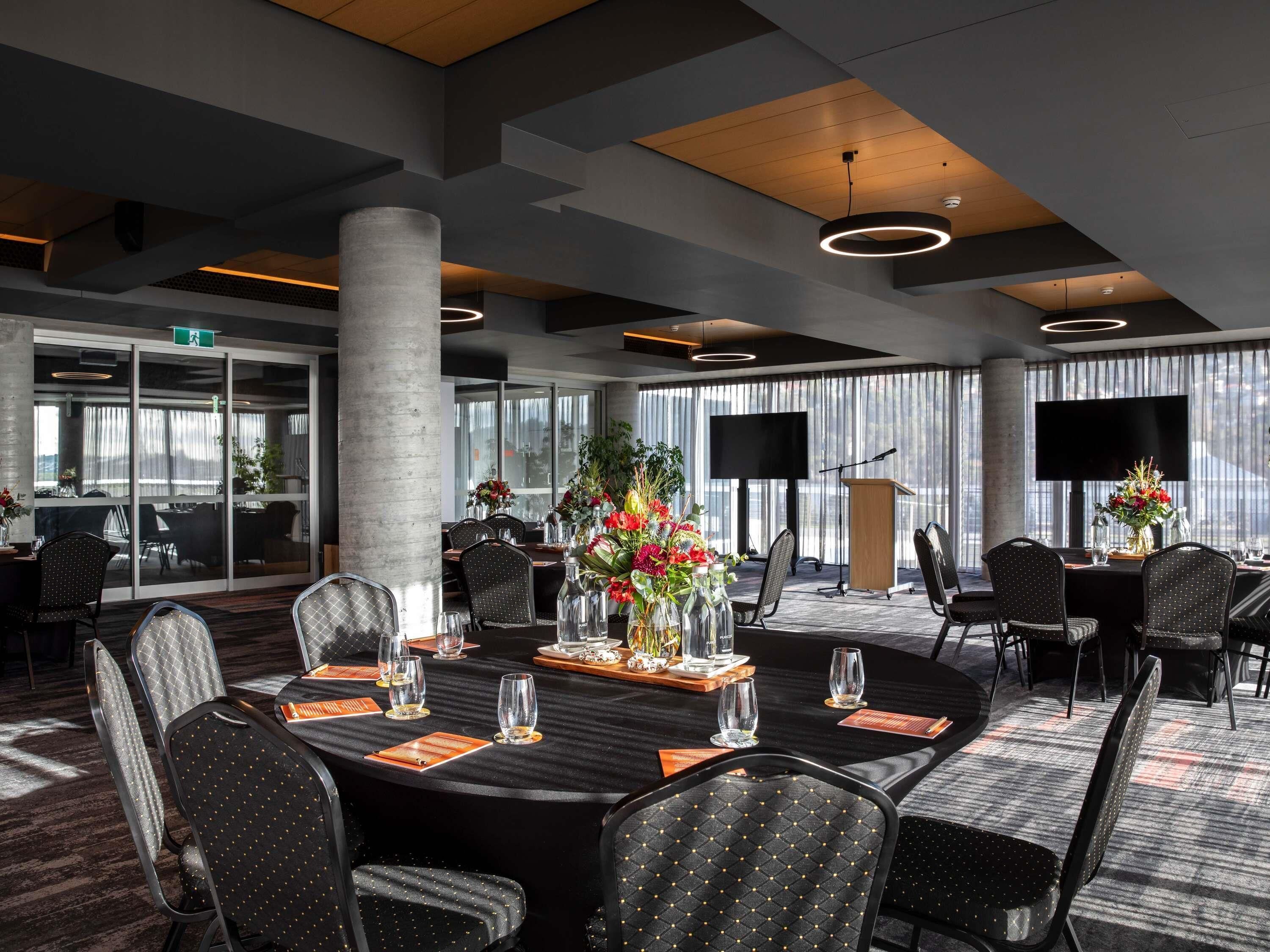 A conference room with round tables, chairs, a large screen, and a podium.