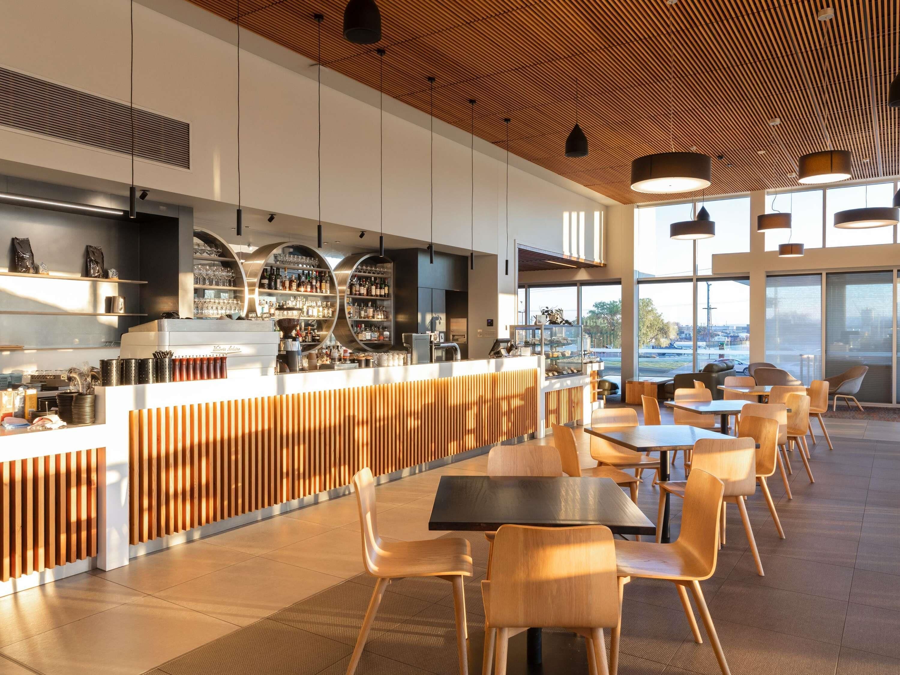 A modern bar area with a wooden ceiling, bar counter with circular shelves, and seating area with tables and chairs.
