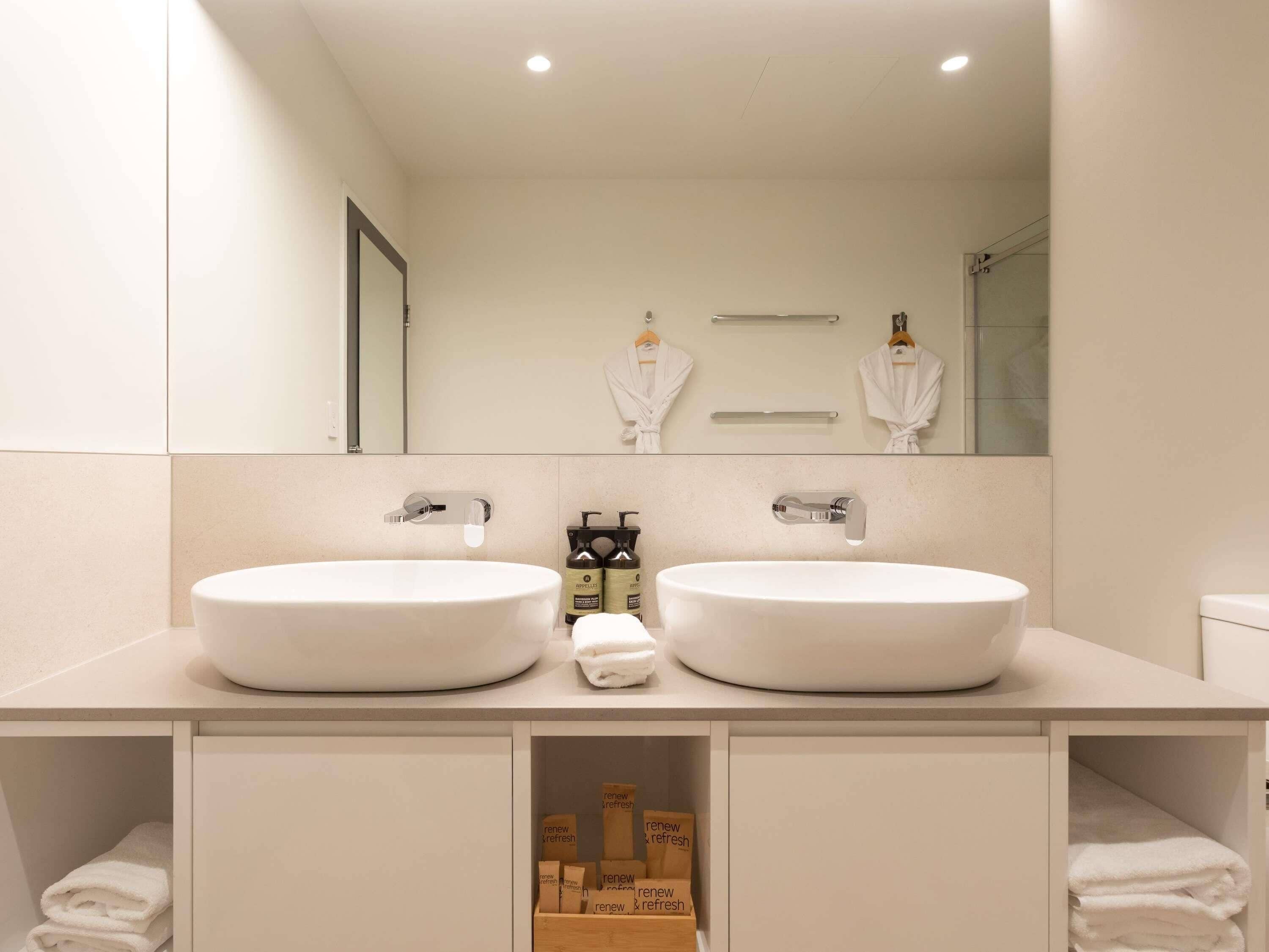 Een moderne badkamer met twee wasbakken, een spiegel en een douche.