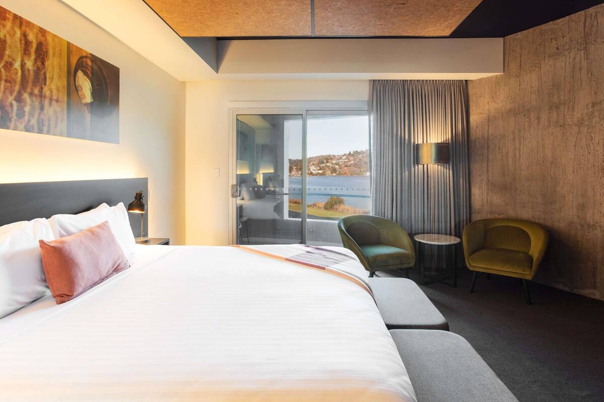 A modern hotel room with a large bed, a view of the outdoors, a balcony, and a seating area.