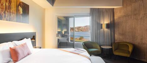 A modern hotel room with a large bed, a view of the outdoors, a balcony, and a seating area.