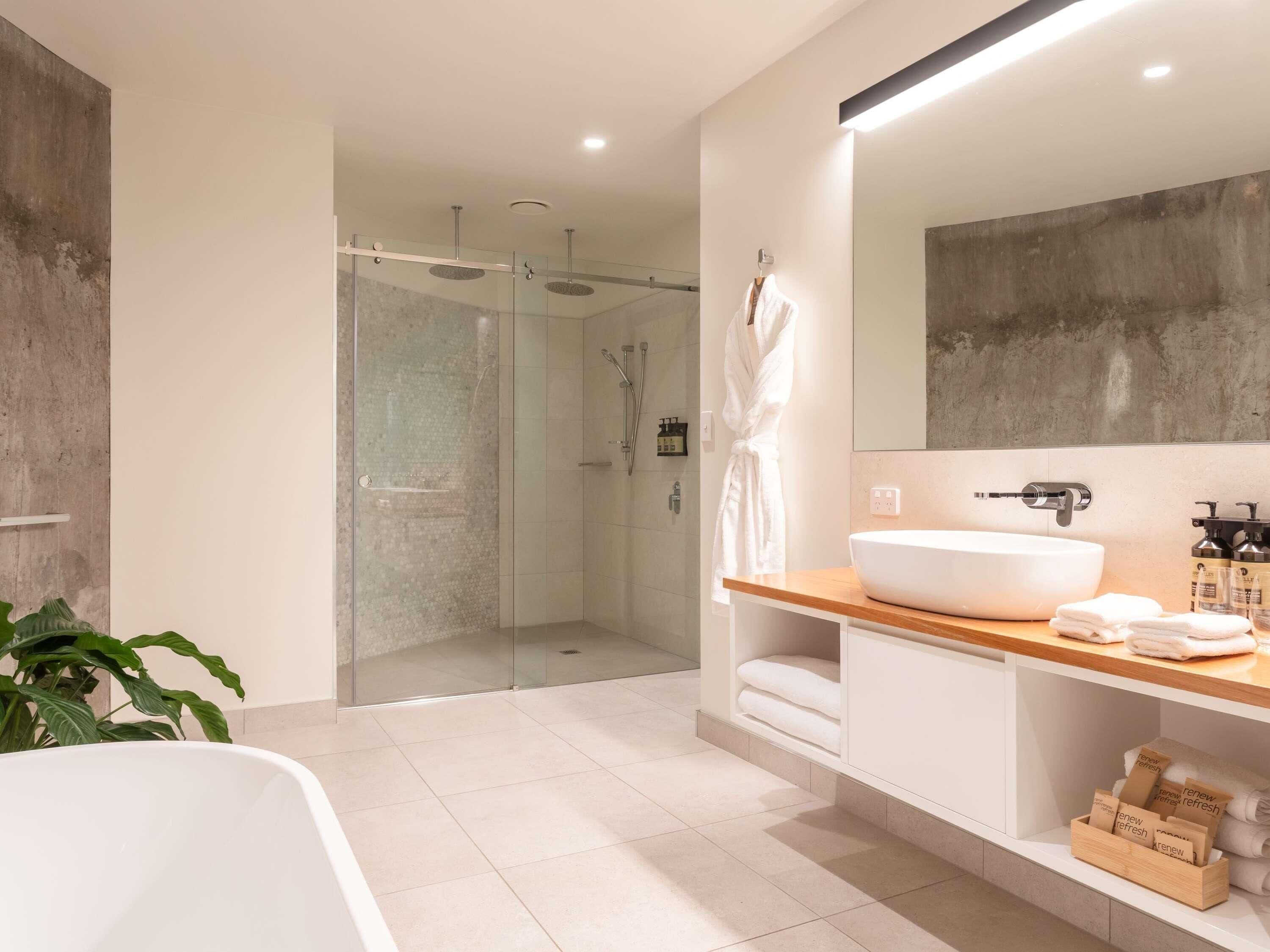 A modern bathroom with a glass-enclosed shower, a white bathtub, and a vanity with a large mirror and a wooden countertop.