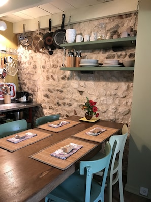 Ein Essbereich mit einer Steinwand, einem Holztisch mit Platzsets und Stühlen, und einer Vase mit roten Blumen auf dem Tisch.
