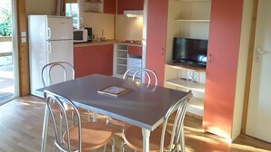 Een compacte keuken met een koelkast, magnetron en een televisie op een plank. Er is een eettafel met stoelen en een raam dat natuurlijk licht biedt.