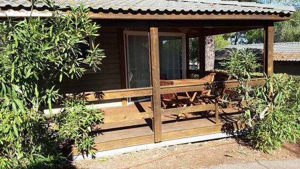 Een houten chalet met een veranda, een eettafel en stoelen.