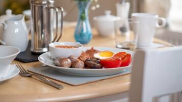Una colazione con un piatto di uova, salsiccia e pomodori, una caffettiera e un vaso di fiori.