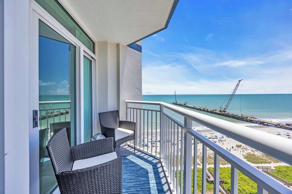 A balcony with wicker furniture, a view of the beach, and a pier with a crane.