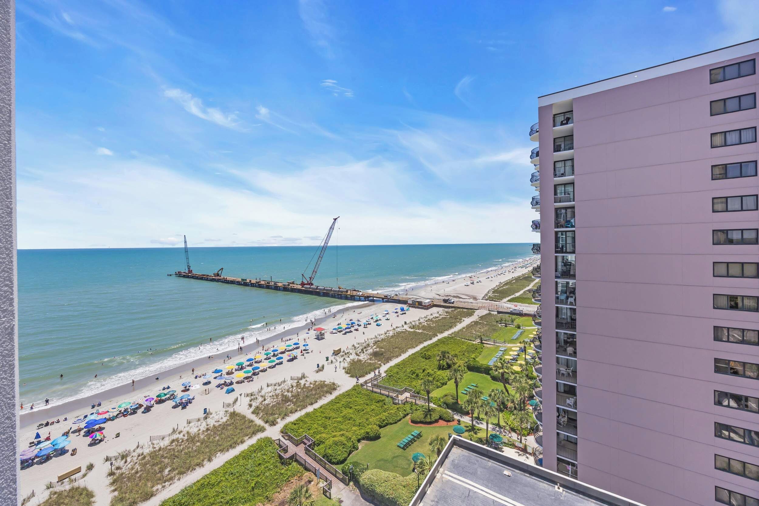 A beach view with a pier, a hotel building, and a well-maintained lawn area.