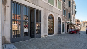 A street with a building featuring large windows and a door with a metal gate. - Ca' degli Archi 2 (Venice)