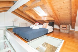 Een slaapkamer met dakraam, houten balken, een bed met kussens, een nachtkastje en een rieten mand.