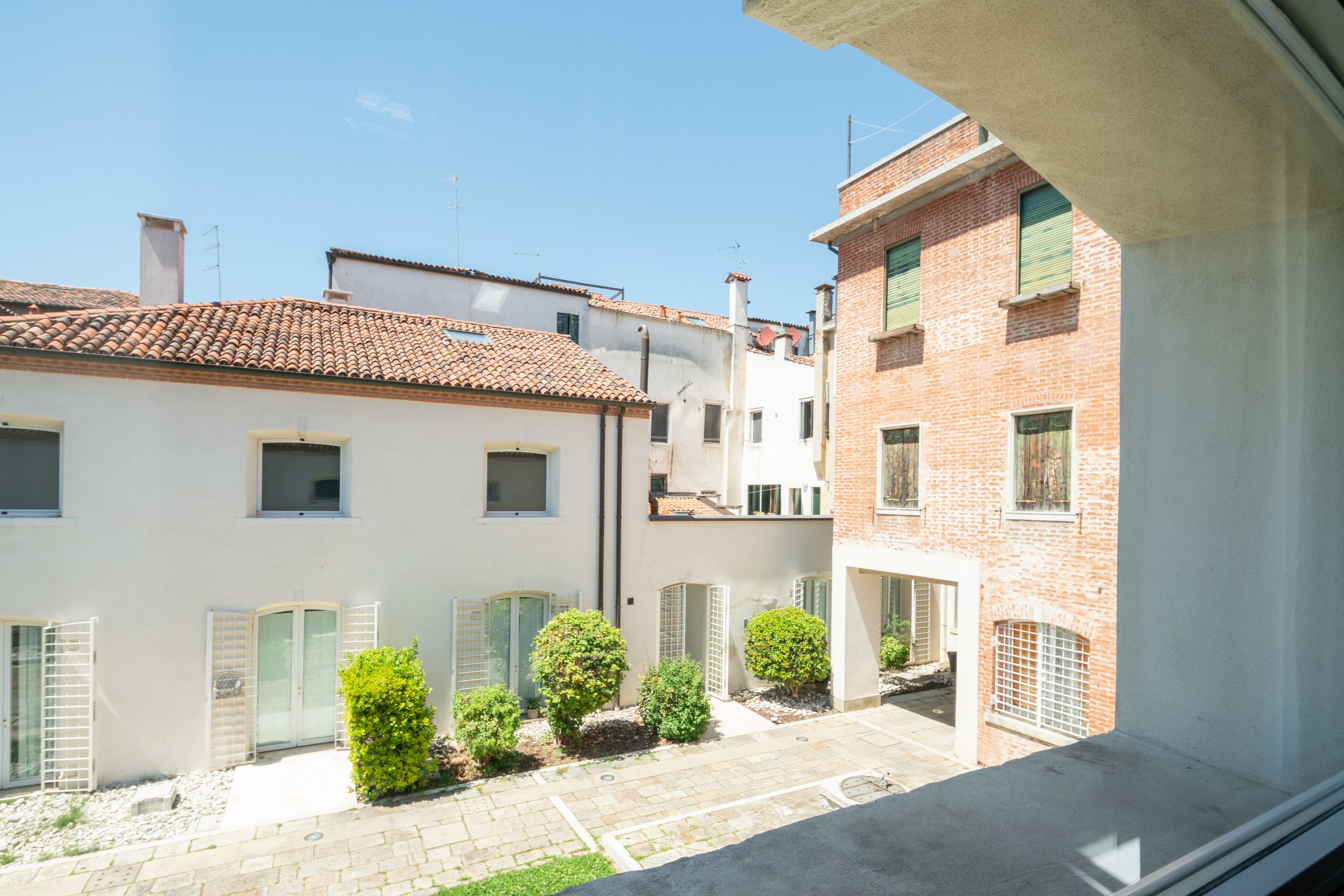 A courtyard with a tiled roof, a white building with a door, and a brick building with a window.