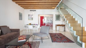 A modern living room with a sofa, a coffee table, and a chair. There is a staircase with glass railings and a wooden finish. - Ca' degli Archi 2 (Venice)