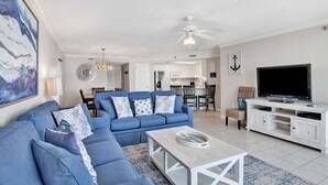 A living room with a sectional sofa, a coffee table, a TV, and a dining area with chairs and a table. - Phoenix VII 803 | Spacious, beach front, clean, comfortable! (Orange Beachg)