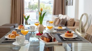A breakfast table with pastries, fruit, and orange juice in a modern hotel room with a view. - Alekos Apartments 1 (Athens)