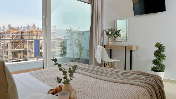 A modern hotel room with a large window, a bed, a desk, and a TV. - Alekos Apartments 1 (Athens)