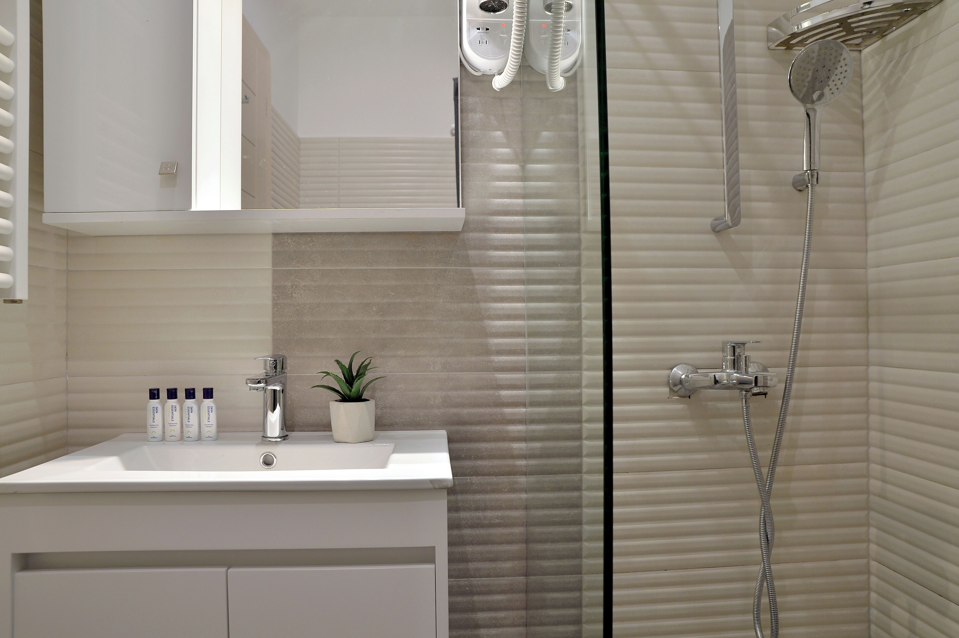 A bathroom with a white sink, a potted plant, and a shower with a glass door.