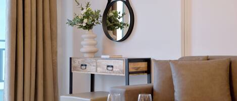 A modern living room with a sofa, a coffee table with two glasses of wine, a vase with flowers, and a wall-mounted mirror.