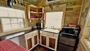 A compact kitchen with wooden cabinets, a stainless steel refrigerator, a microwave, and a window with a view.