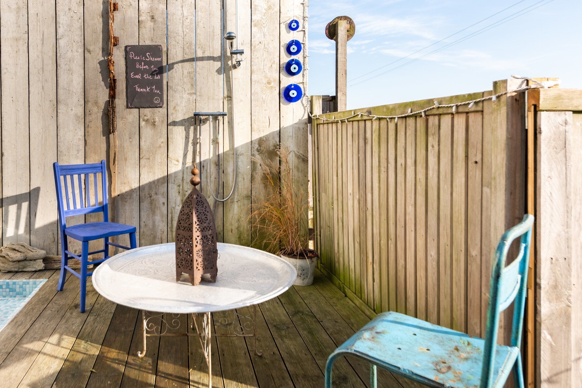 An outdoor patio with a round table, two blue chairs, a wooden fence, and a sign on the wall.
