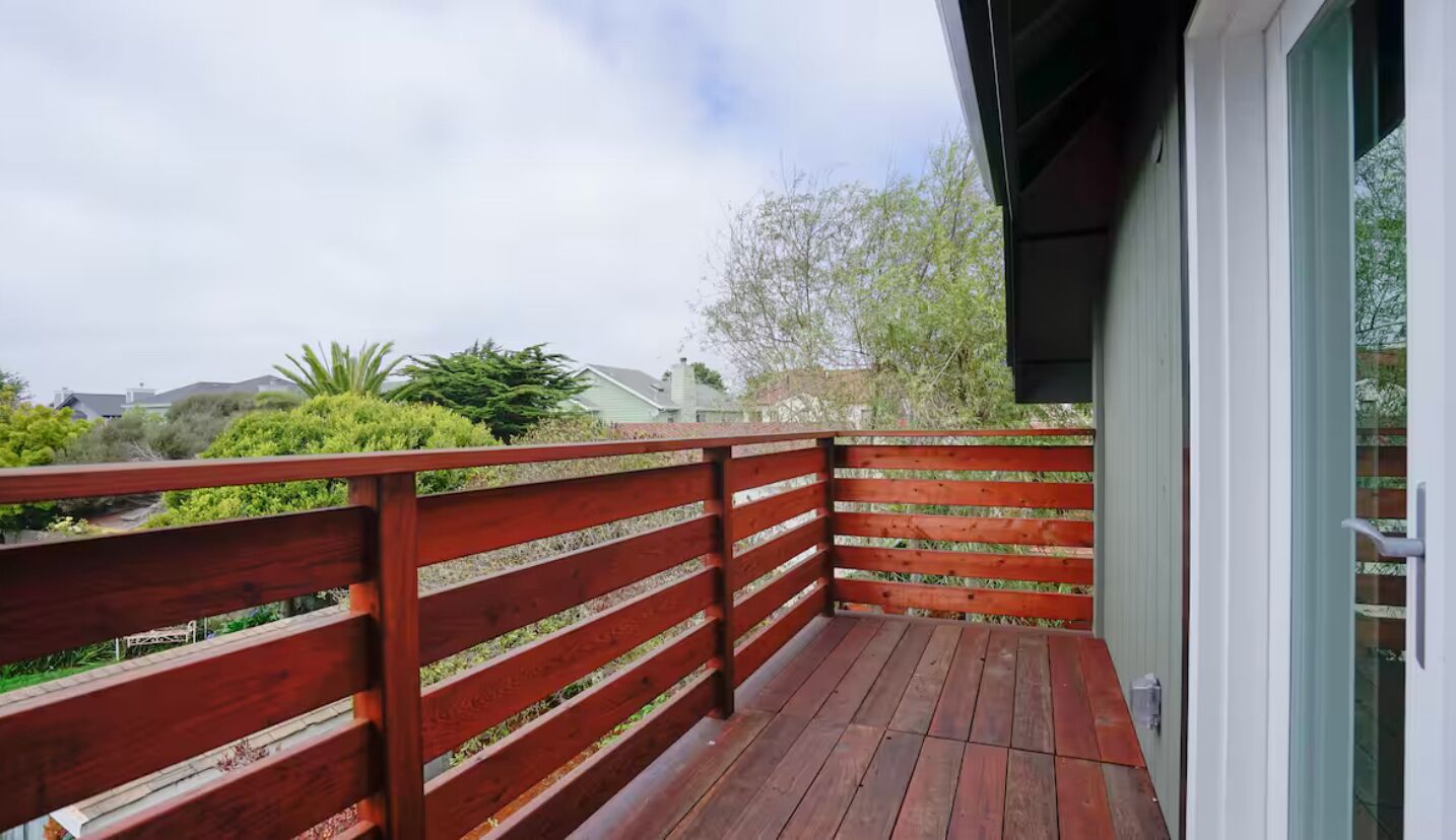 Eine Holzterrasse mit Metallgeländer, die auf einen Garten mit verschiedenen Pflanzen und Bäumen blickt.
