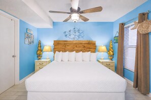 A bedroom with a wooden headboard, a ceiling fan, two bedside tables with lamps, and a window with curtains.