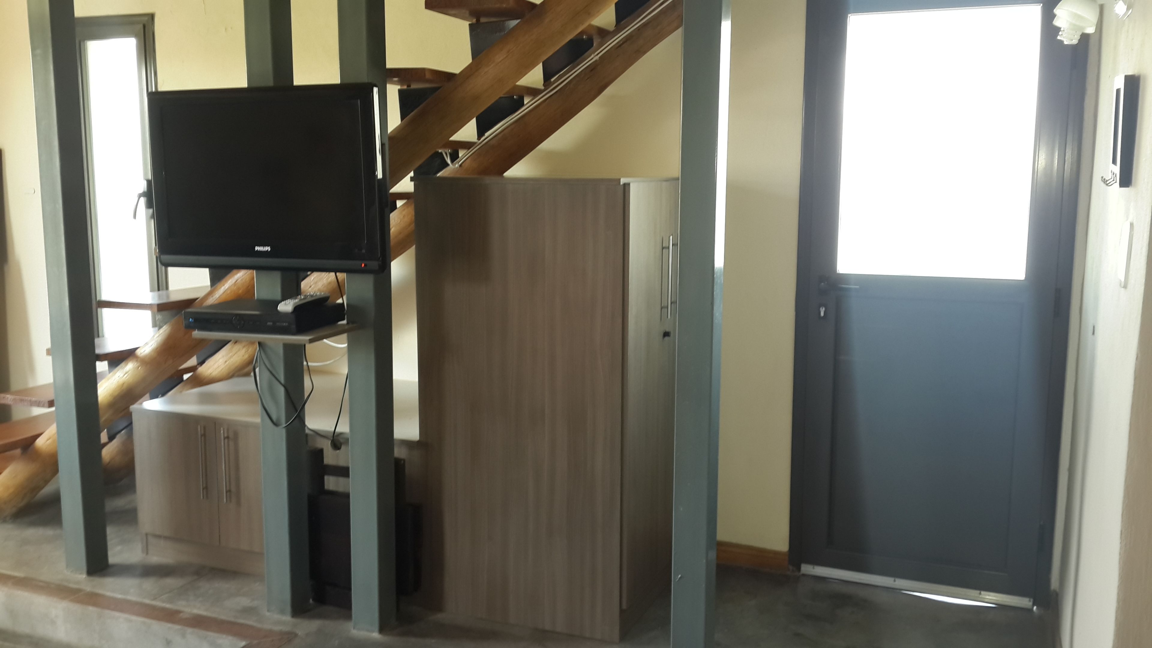 A room with a staircase, a television mounted on a stand, a wardrobe, and a door.