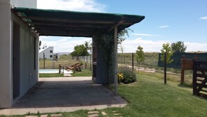 Zona de porxo coberta amb sòl de formigó, piscina al fons i pati tancat amb vegetació escassa.