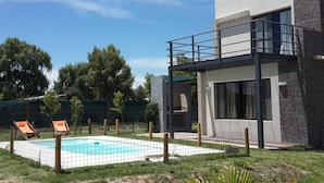 Una casa moderna de dues plantes amb una piscina, un balcó i un jardí tancat per una tanca.