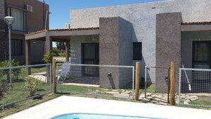 Edifici modern amb zona de piscina, tanca metàl·lica, un petit jardí i un cel serè.