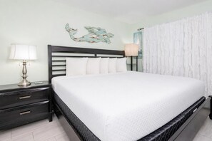 Een net opgemaakt bed met witte lakens, een donker hoofdbord en een nachtkastje met een lamp.