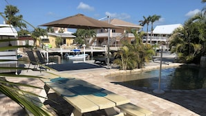 A poolside area with a wooden picnic table, lounge chairs, and umbrellas.