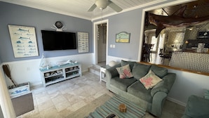 A living room with a grey couch, a flat-screen TV, a fish-themed wall art, and a ceiling fan.