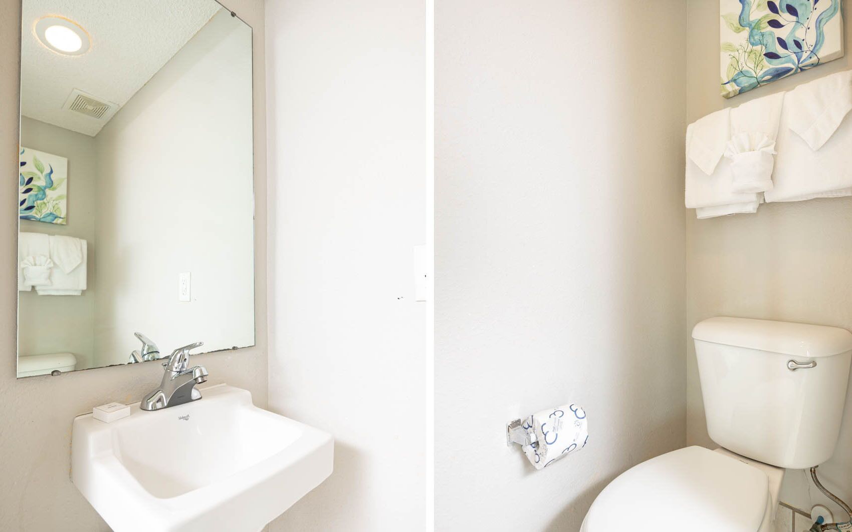 A bathroom with a white sink, mirror, and toilet. There is a towel rack above the toilet and a painting on the wall.