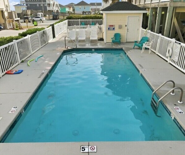 A rectangular pool with a white fence, a small building, and a few chairs. - A Paradise Inn G – Your Topsail Island Escape (Surf City)