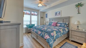 Ein Schlafzimmer mit einem Bett, Nachttischen, einem Deckenventilator, einem Fenster mit Vorhängen und einer Wandleuchte.