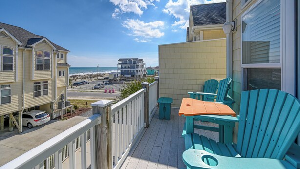 Ein Balkon mit Sitzgelegenheit, Blick auf den Strand und ein Parkplatz mit einem weißen Auto.