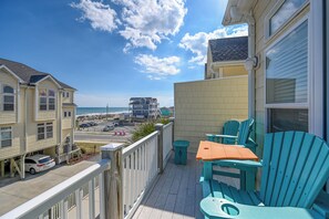 A balcony with outdoor seating, a view of the beach, and a parking area with a white car. - A Paradise Inn G – Your Topsail Island Escape (Surf City)