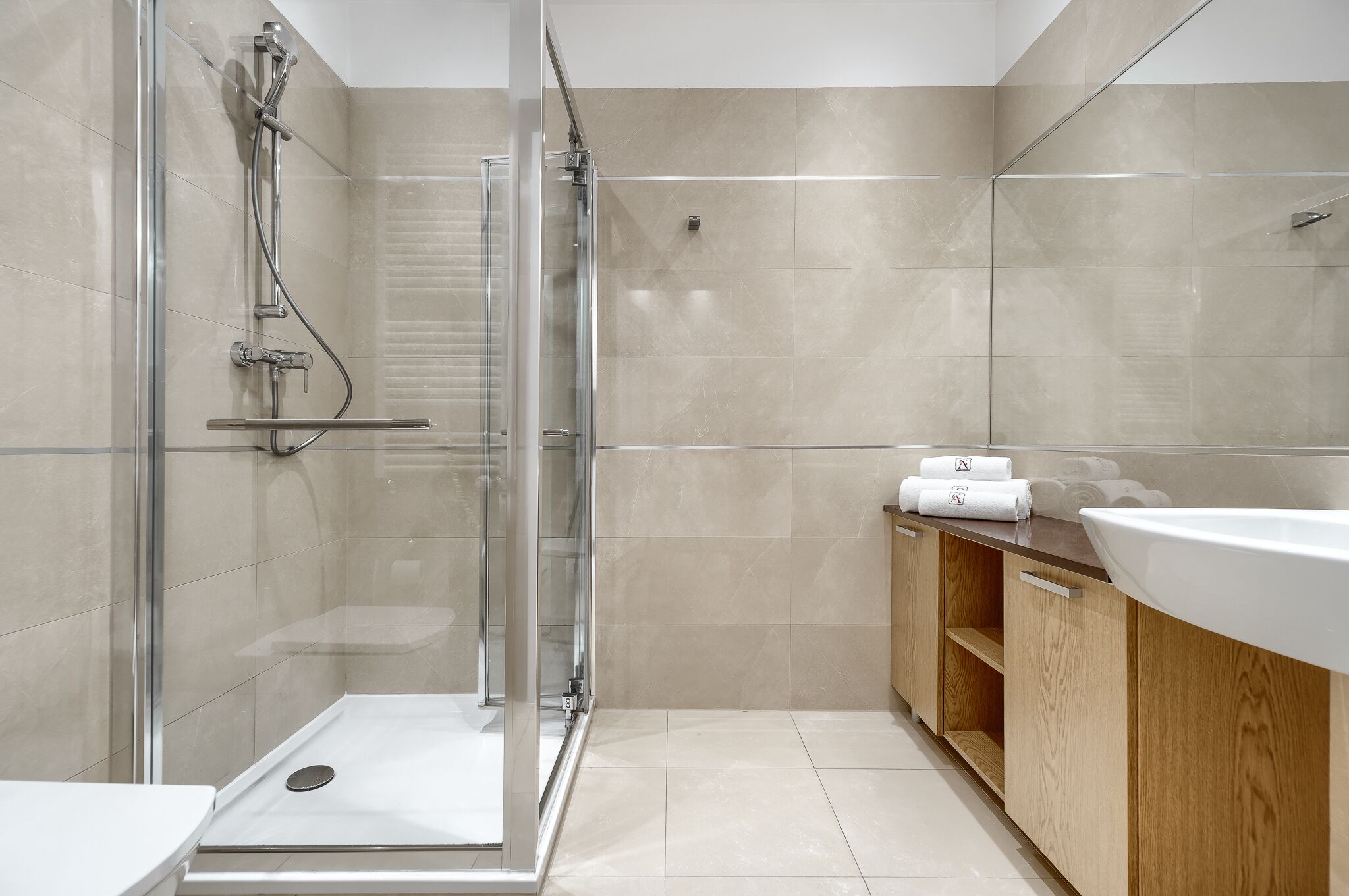 Une salle de bain moderne avec une douche à parois de verre, un meuble-lavabo en bois avec un évier blanc et des murs recouverts de carreaux beiges.