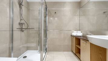 Une salle de bain moderne avec une douche à parois de verre, un meuble-lavabo en bois avec un évier blanc et des murs recouverts de carreaux beiges.