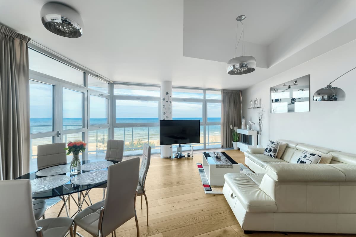 Un salon moderne doté d’un grand téléviseur, d’un canapé, d’une table à manger avec des chaises et offrant une vue sur la mer.