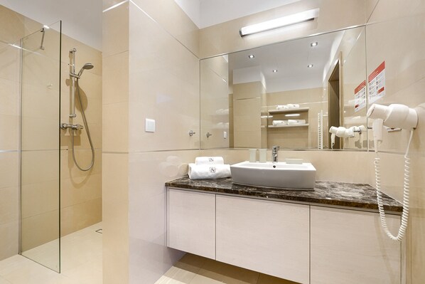 Un baño moderno con ducha envuelta en vidrio, un lavabo con encimera de mármol y un espejo con toallero.