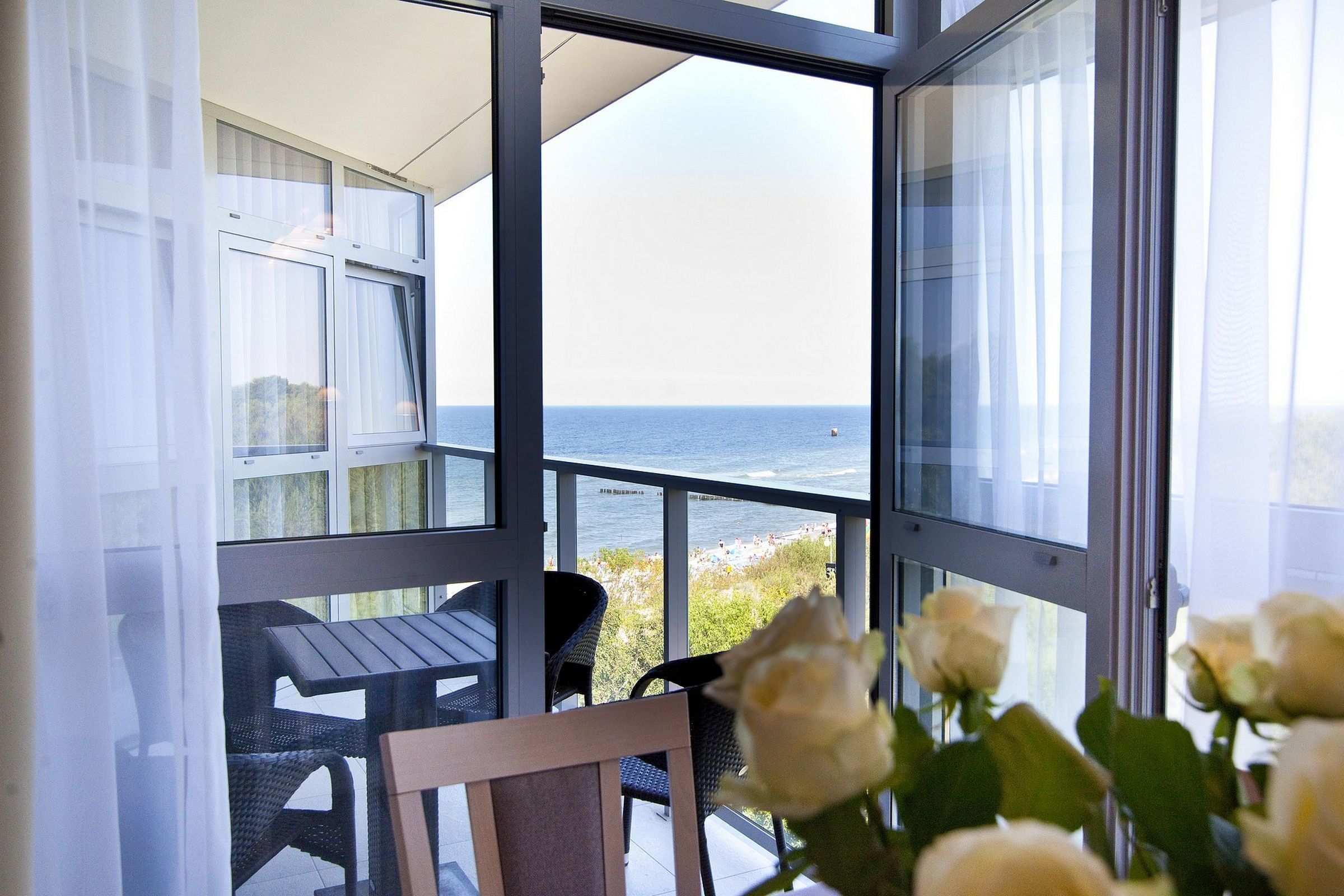 Un balcón con vista al mar, una mesa, sillas y un jarrón con flores.