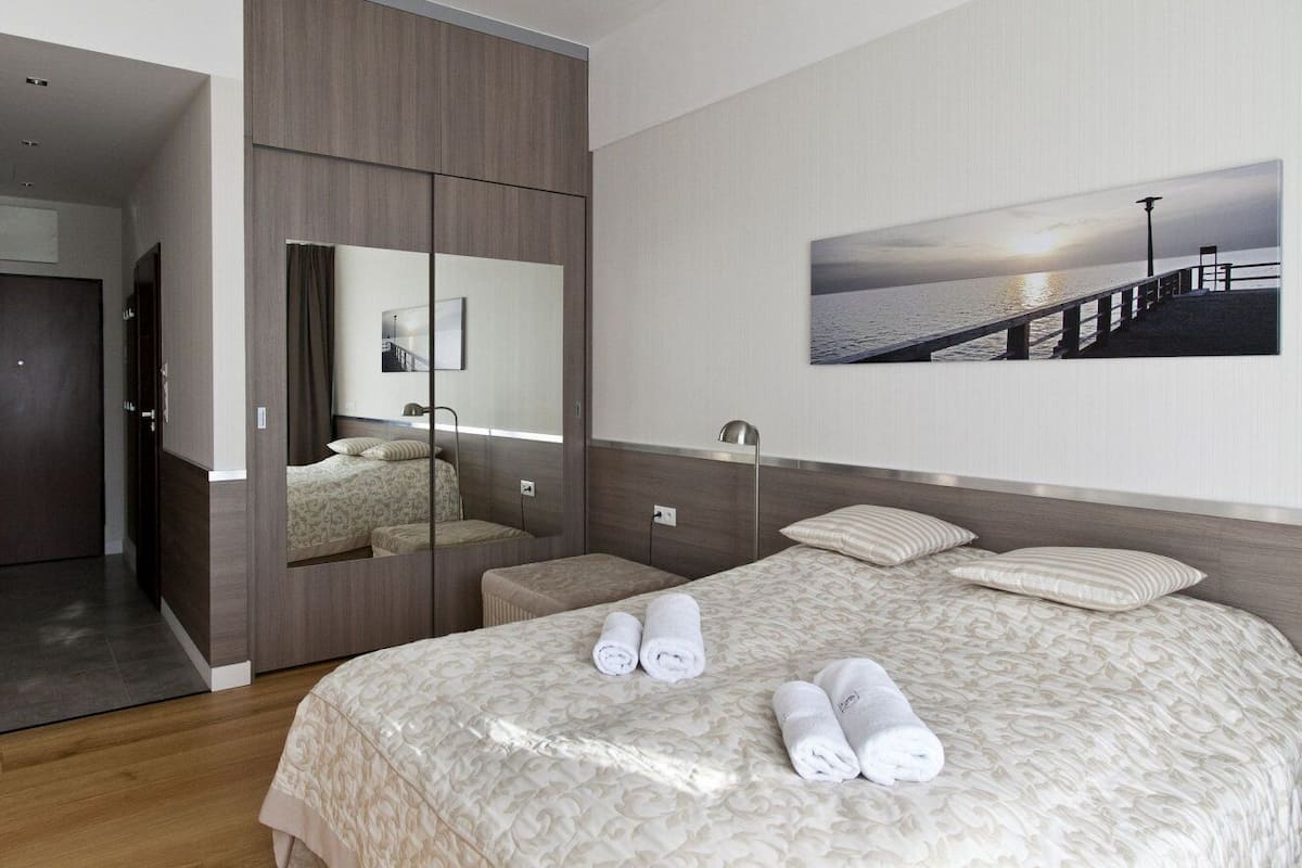 Une chambre d’hôtel avec un grand lit, un miroir, une table de chevet et une vue sur la mer par la fenêtre.