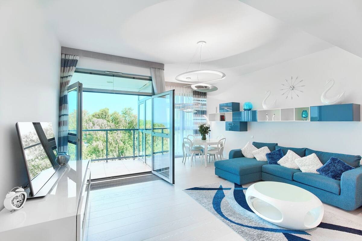 Un salon moderne avec un canapé bleu, une table basse blanche et un coin repas comprenant une table et des chaises blanches.