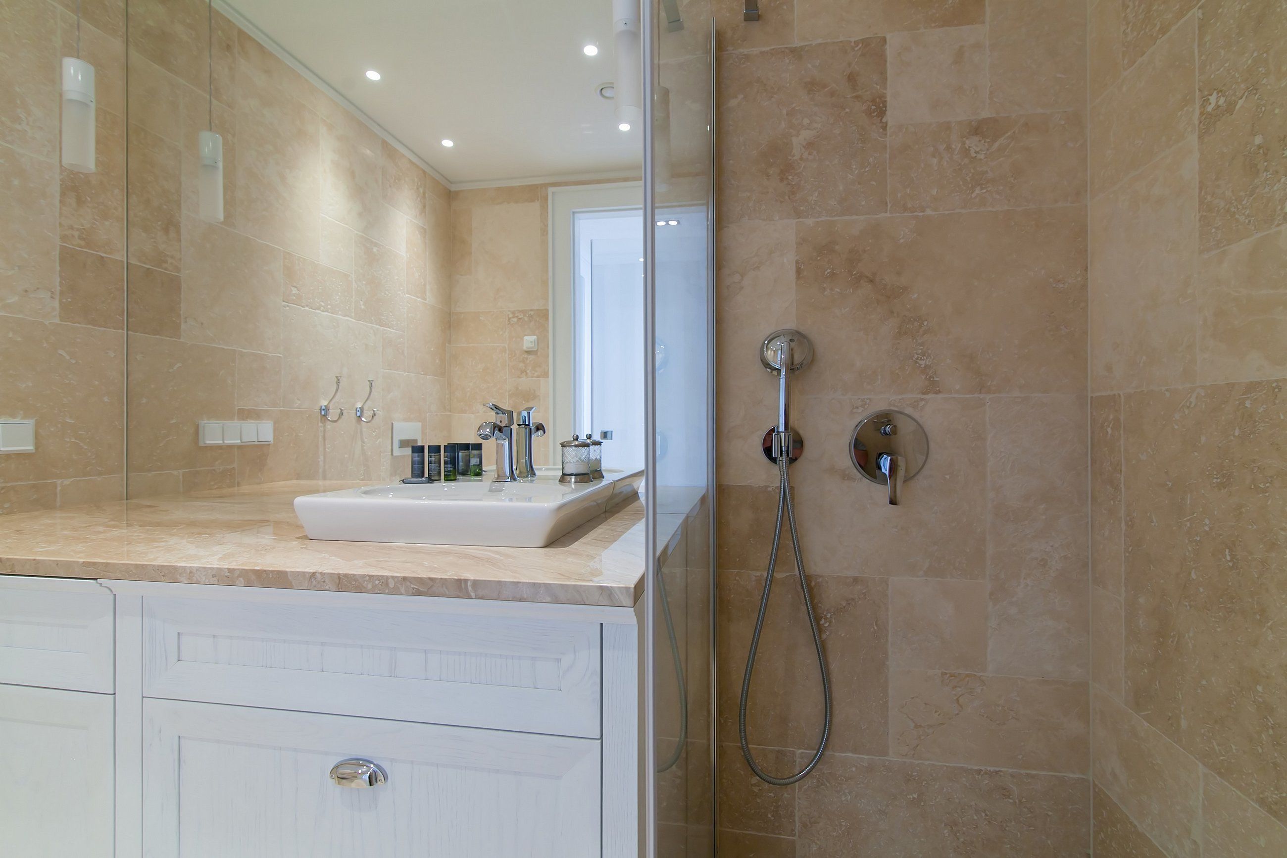 A modern bathroom with a glass-enclosed shower, a white sink, and beige tiles.