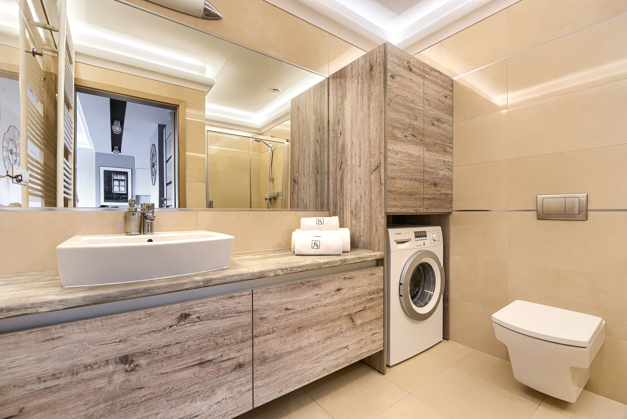 A modern bathroom with a wooden vanity, a built-in washing machine, and a toilet.