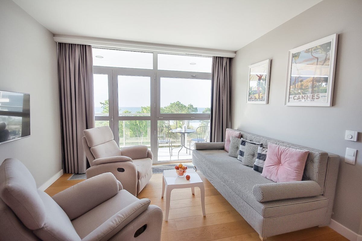 Un salon moderne avec un canapé, des fauteuils, une table basse et une vue sur l’extérieur.